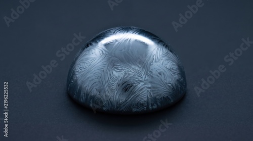 Solid tantalum metal ingot with crystalline surface texture isolated on a dark grey background
