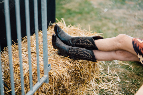 Fotografía Legs Resting on Hay Bale Near Fence at Country Event
