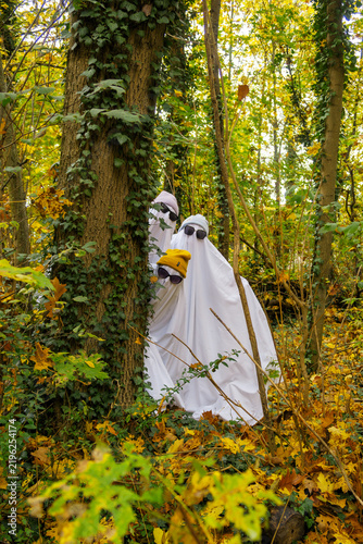 Three Halloween sheet ghosts peeking from behind tree in forest