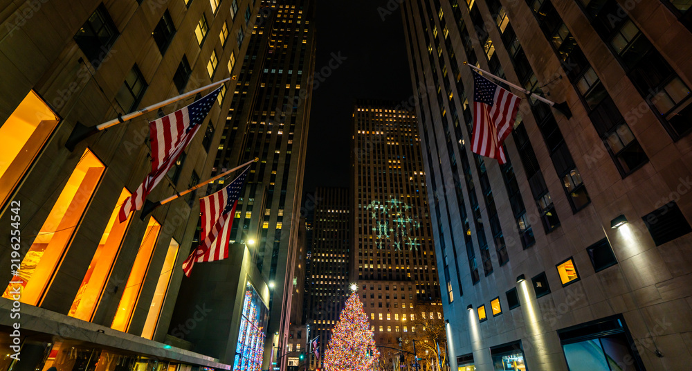 Obraz premium Christmas tree in NYC glowing during winter night. Winter holiday in New York festive city scene. New York winter atmosphere with Christmas decorations. New York City Christmas season downtown.