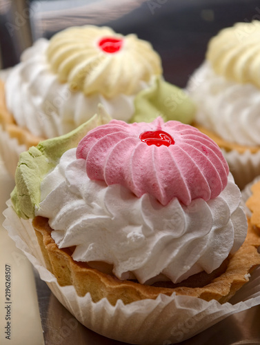 Cream and marshmallow pastries with a light airy texture presented in white paper wrappers on a pastry shop display, showcasing delicate sweet desserts with a soft look