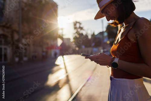 Close-up. a young woman holding a smartphone and typing a message. She is using the phone outdoors against a cityscape background.
