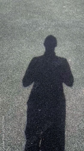 A clear shadow of a standing person on gray asphalt in bright sunlight. A minimalist plot with a lot of free space.
