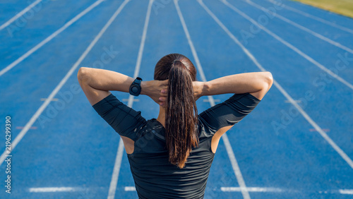 Rear view of female runner warming up before a run with hands on head, woman athlete exercising in track and field stadium, sports training, fitness workout, active lifestyle and race preparation