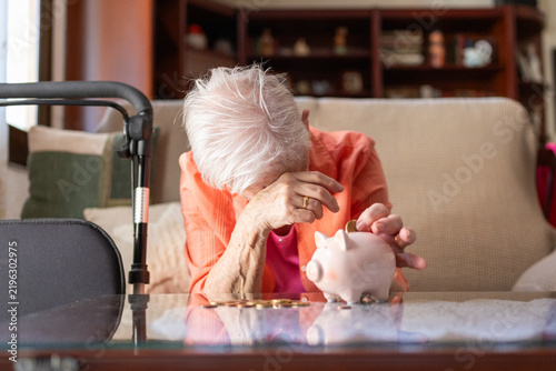 Fotografía Elderly woman at home placing a coin into a piggy bank