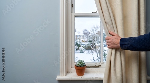 Hand opening curtains to look out of a bright home window