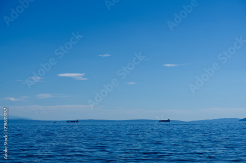 Distant cargo ships sailing on the calm blue sea under a wide bright sky