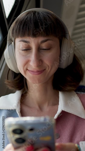 Woman in earphones travels by train. young woman wearing earphones and looking at her phone in the train. headphones and phone.  
