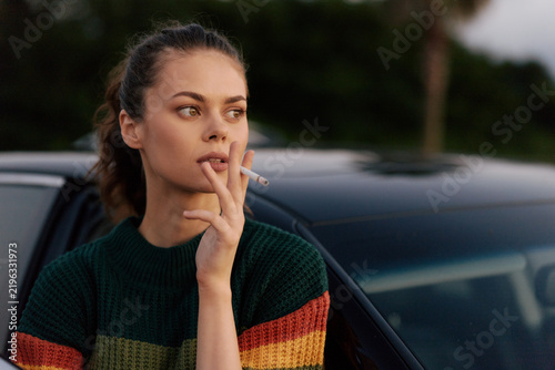 Fotografie Young woman smoking cigarette outdoors near car