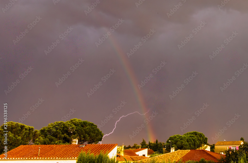 Obraz premium Un éclair d'orage croise l'arc en ciel au dessus du village