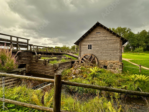 Old Wooden Watermill with Stone Foundation in a Rural Landscape Under a Dramatic Sky