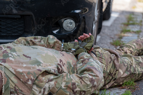 Fotografie Soldier in camouflage uniform lies beside a car with his hands restrained in handcuffs after detention
