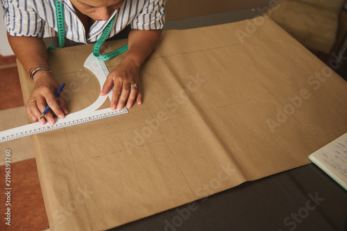 Woman drafting sewing pattern on kraft paper with measuring tape and ruler in a home studio