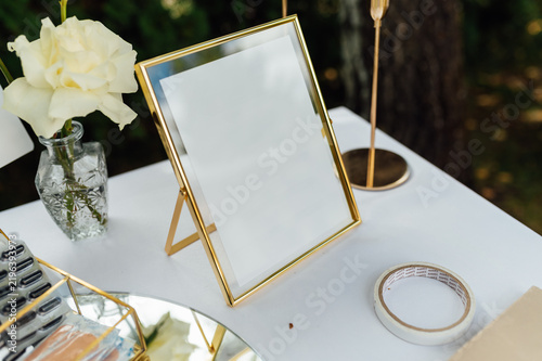 Blank gold photo frame mockup on wedding table with white rose.