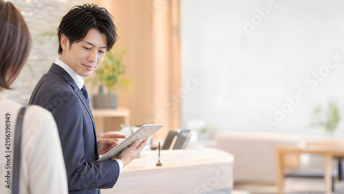 カスタマーサービス素材として使いやすい受付カウンターでタブレットを確認する男性スタッフ 柔らかな光と広いコピースペース