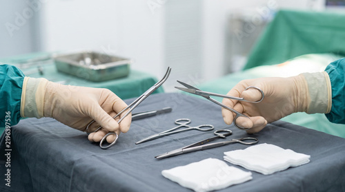 Gloved surgeon hands hold scissors and forceps over sterile tray with surgical tools in OR