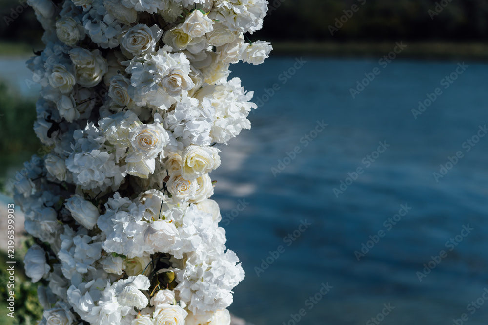 Fototapeta premium White rose floral arch detail for outdoor wedding ceremony by the lake.