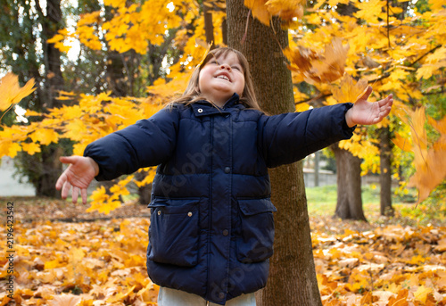 Happy little girl throwing autumn leaves up. Motion blur effect.