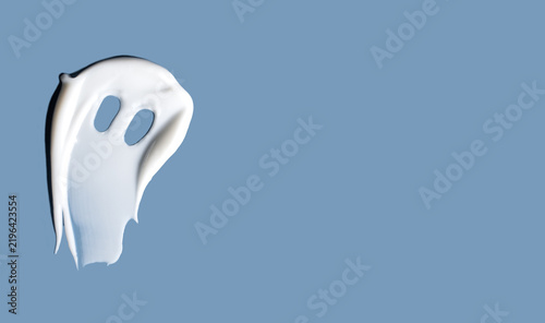 Halloween beauty concept with ghost shaped cosmetic cream stroke and copy space on blue background