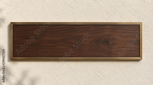 Blank horizontal wooden plaque with elegant bronze frame mounted on a textured plaster wall with soft natural leaf shadows, perfect for logo mockup or office nameplate branding.
