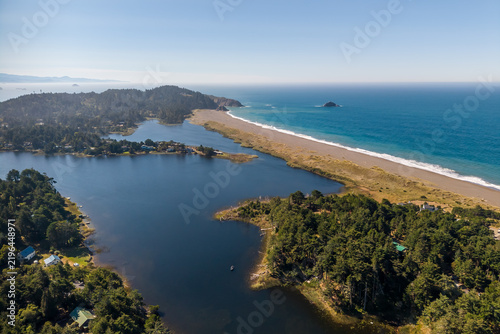 Aerial view of Garrison Lake separated from the Pacific Ocean by a sandy beach, surrounded by dense evergreen forests and coastal terrain in Port Orford, OR, United States.