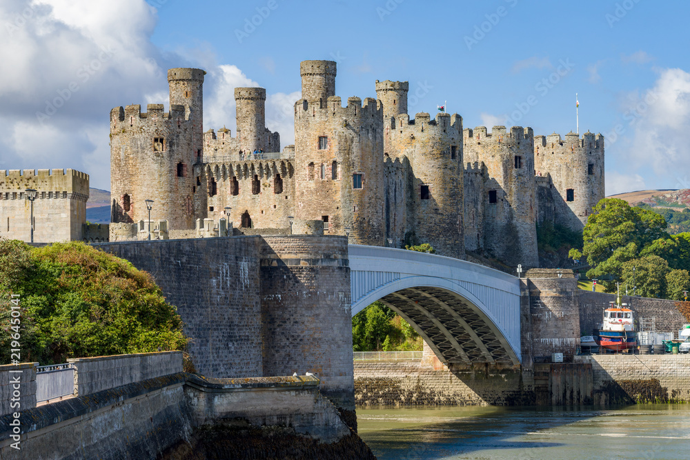 Obraz premium Medieval stone fortress towers and arched road bridge over tidal river estuary, historic coastal defensive fortification on sunny day