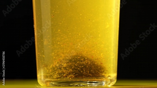 фотографія A clear glass filled with yellow herbal infusion on black background