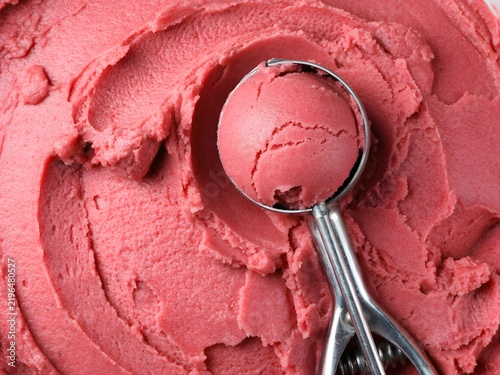 Scoop of strawberry ice cream in cone with spoon on pink swirl background