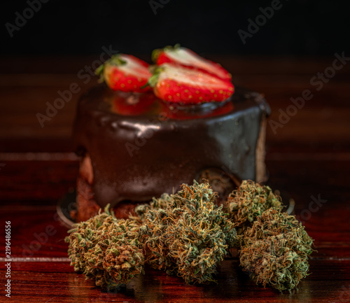 Chocolate strawberry fruit brown cake wooden table with marijuana flower blooms