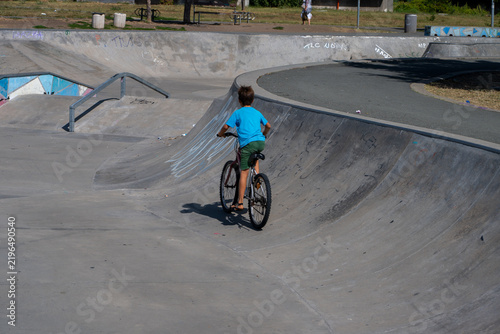 Quadro su tela A young boy on a bicycle rides up an inclined ramp beside metal grind rails at a concrete outdoor skatepark