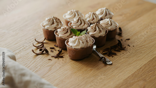 chocolate mousse in small clear plastic cups. Sweet dark cocoa dessert with creamy swirl, chocolate shavings on light wooden table. Tasty mini pudding treats for party, created with generative ai