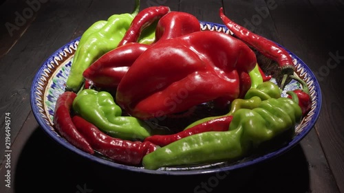 Large red and green peppers in a bowl spin on a table against a dark background.