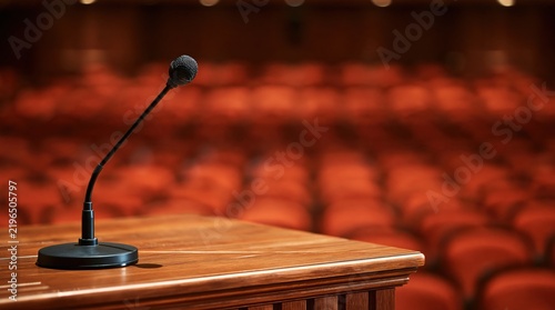 Microphone on wooden podium in empty auditorium with red seats in background