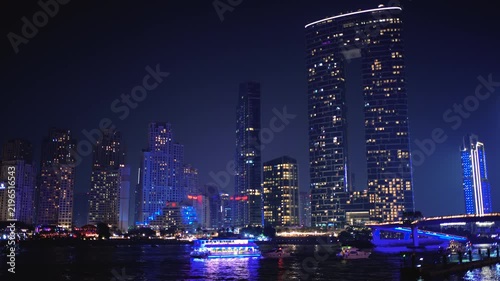 The lights of the Dubai Marina at night. A boat cruises through the bay.