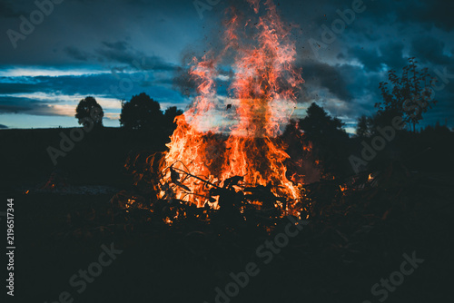 vivid fire illuminates the darkness with a dramatic sky and silhouetted trees in the background