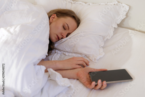 Фотография Smartphone Addiction and Sleep Disruption as Woman Falls Asleep Holding Phone