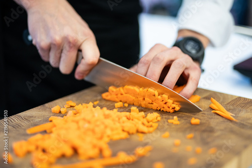 Foto Chef finely dicing a carrot on a wooden cutting board