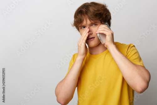 Konstfotografi Young man in yellow shirt making phone call and expressing doubt and annoyance while listening closely