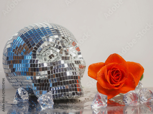 Foto Shiny disco ball skull beside red rose on reflective surface