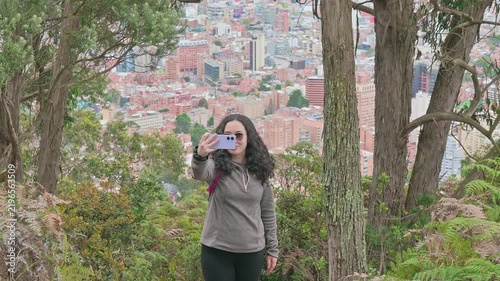 Woman Taking Selfie While Hiking Above City With Panoramic Urban View and Forest Trail