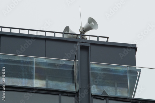 Fotografía Public address horn loudspeakers on a modern building roof against a grey sky