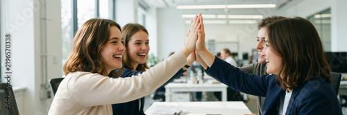 Brown-haired women with fair skin tones sitting at a table and stacking hands in celebration.