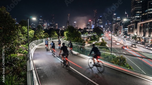 Group of cyclists riding on urban cycleway at night with city lights in background