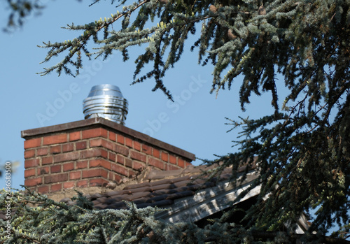 Red brick chimney has a shiny metal vent atop it