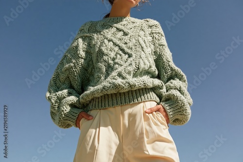 woman wearing an oversized sage green cable knit sweater against a clear blue sky