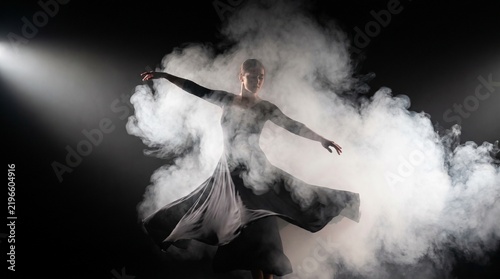 Ballerina dancing gracefully surrounded by dramatic smoke and spotlight on a dark stage