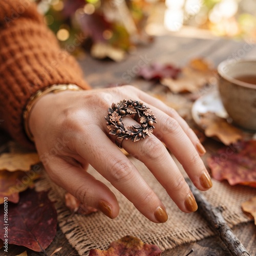 A person wearing a decorative bronze leaf wreath ring while sitting at an autumn table with woman wears detailed metallic ring wreath autumn leaves acorns her finger