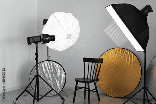 Different modern lighting equipment and chair in photo studio