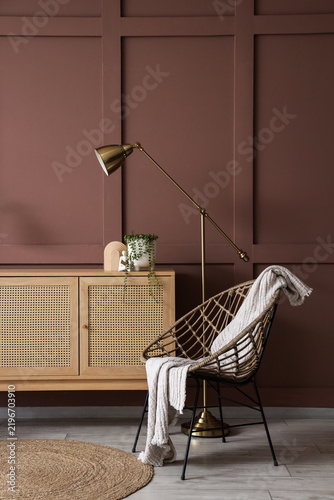 Chest of drawers, armchair and lamp near brown wall in interior of living room, closeup