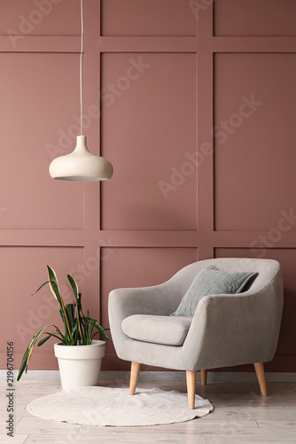 Soft grey armchair with houseplant and hanging lamp near brown wall